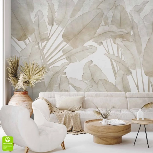 Beżowa tapeta na ścianę do salonu z liśćmi w beżowej tonacji przedstawiająca motyw bananowca, zdobiąca ścianę nowoczesnego wnętrza z jasną sofą, designerskim fotelem i naturalnymi dodatkami w stylu boho.